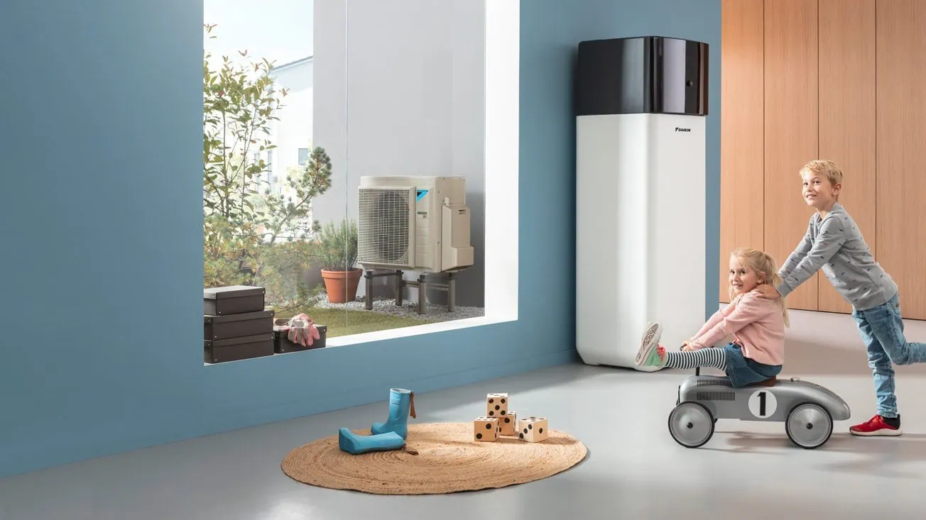 Zwei Kinder spielen neben einer weißen Daikin Altherma 3 R in einem hellen Raum, während draußen am Fenster ein weiteres Außengerät zu sehen ist.